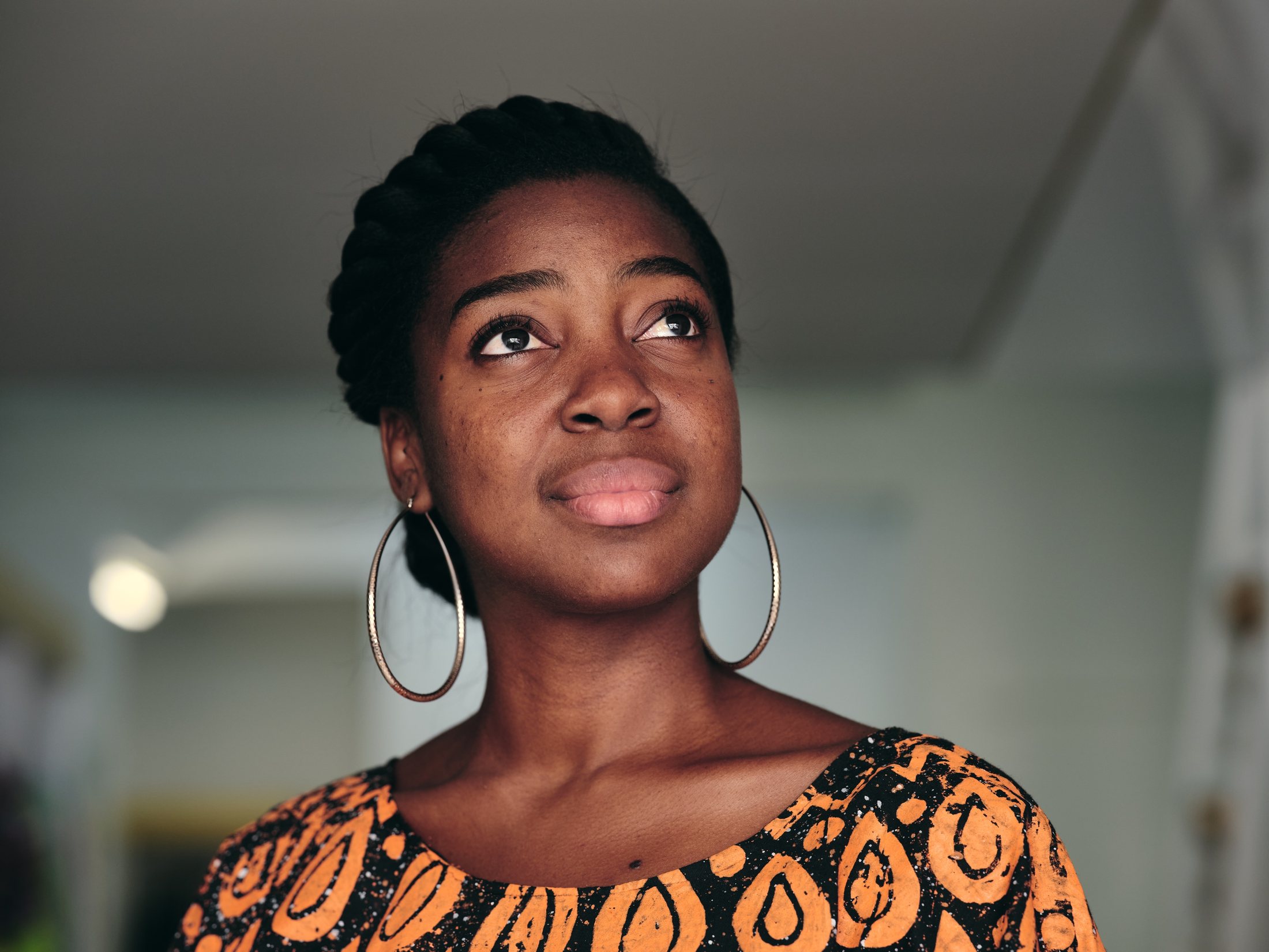 Portrait — jeune femme à la couronne tressée et grandes créoles, regard levé vers la lumière — photographie Romain Cruse