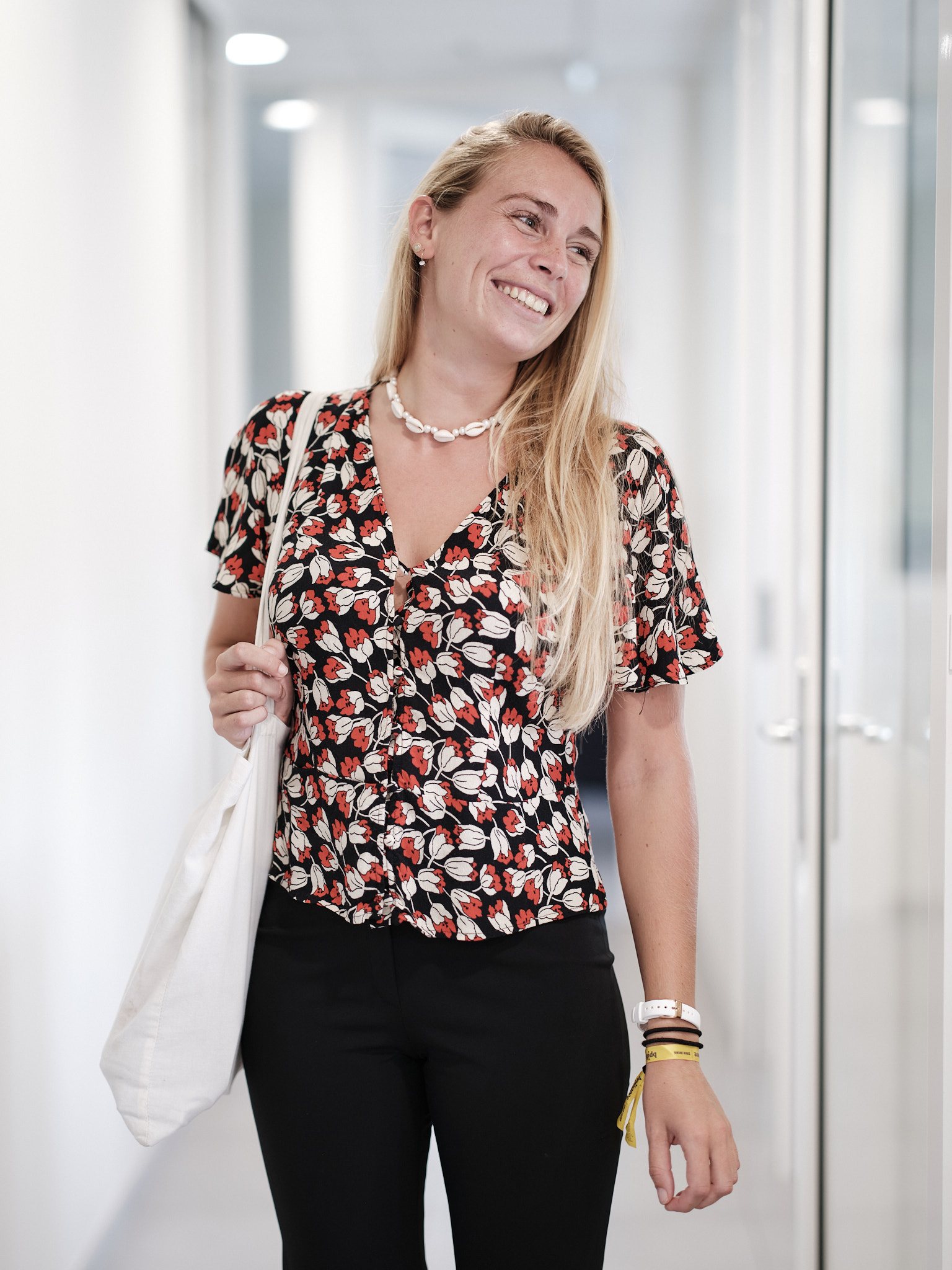 Portrait corporate — jeune femme riant dans un couloir de bureaux, sac de toile à l'épaule — photographie Romain Cruse