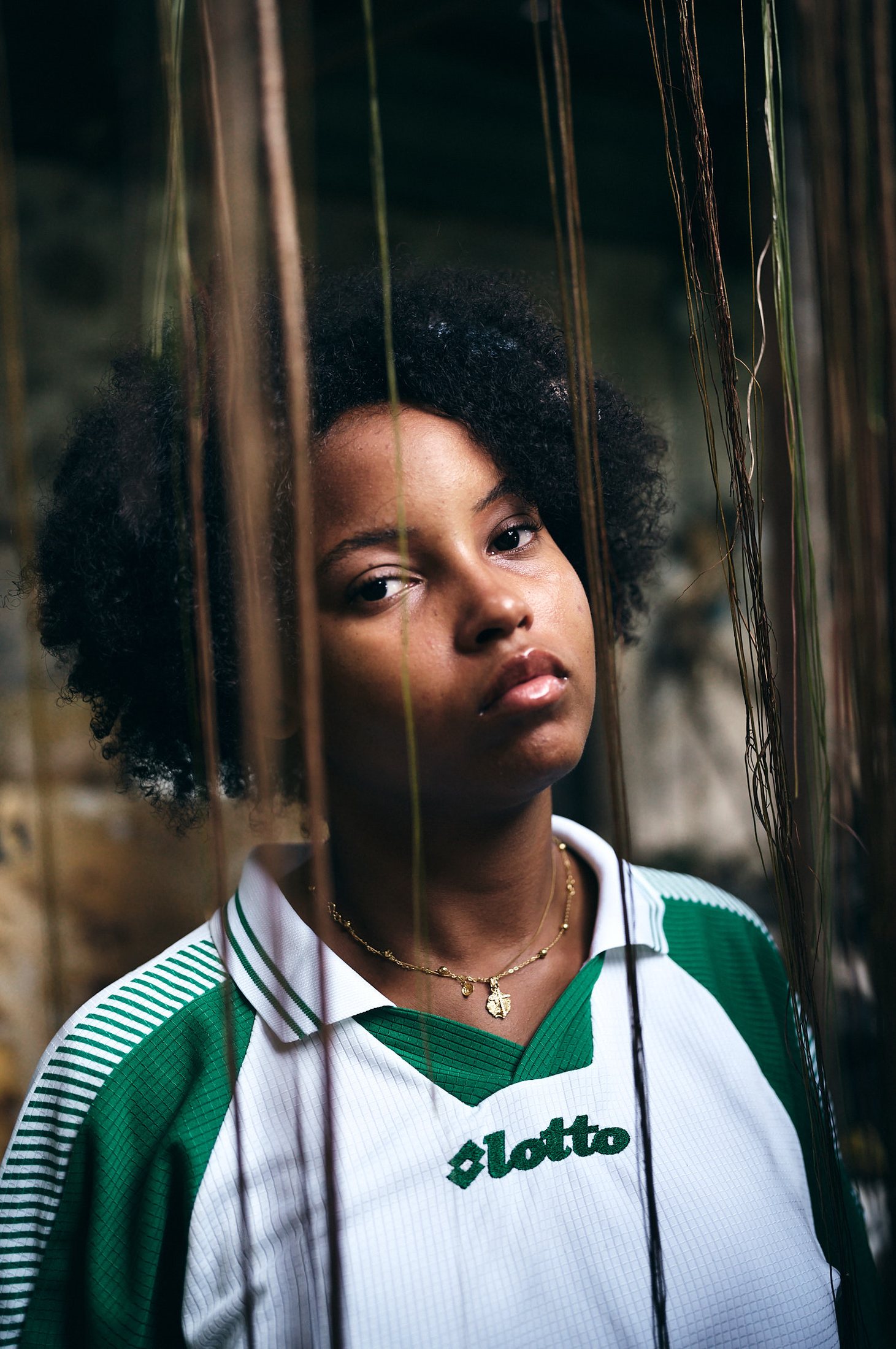 Portrait — jeune femme en maillot de football derrière un rideau de fibres végétales — photographie Romain Cruse