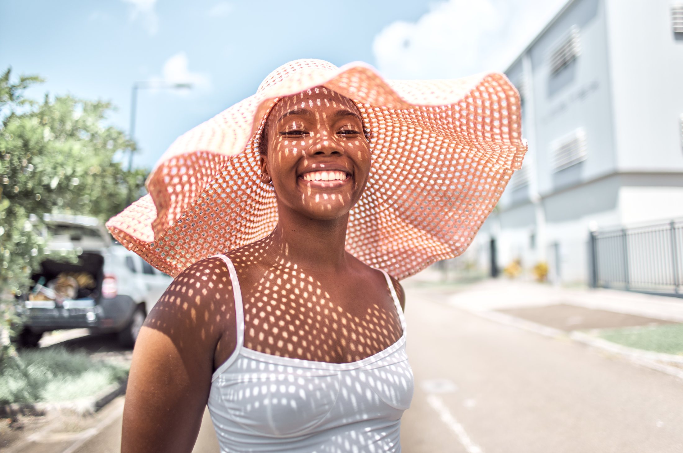 Portrait — jeune femme riant sous un grand chapeau de paille, lumière tramée par le soleil — photographie Romain Cruse