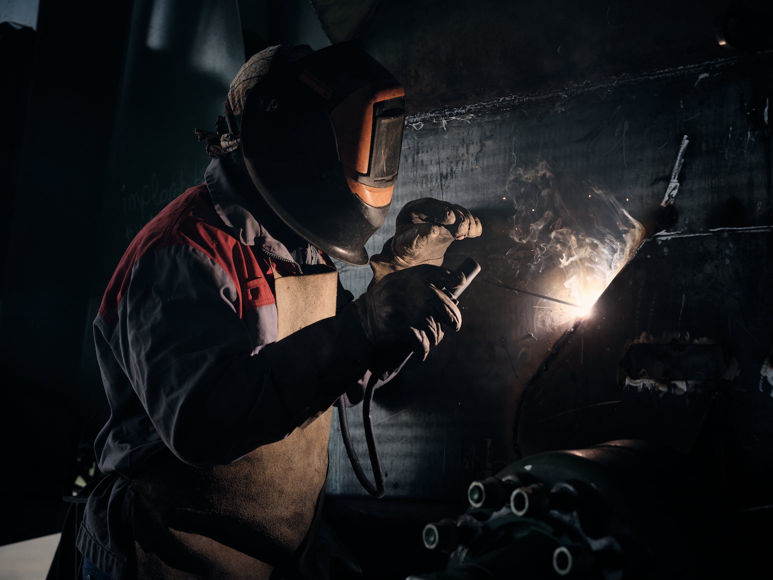 Portrait de métier — soudeur à l'arc dans la pénombre d'un atelier, gerbe d'étincelles — photographie Romain Cruse