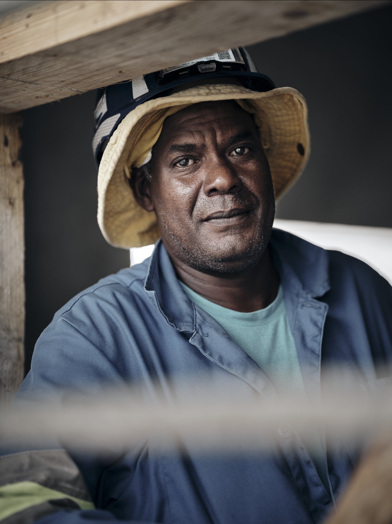 Ouvrier de chantier, bob posé sur le casque, encadré par les bois de coffrage — série Les gars, photographie Romain Cruse