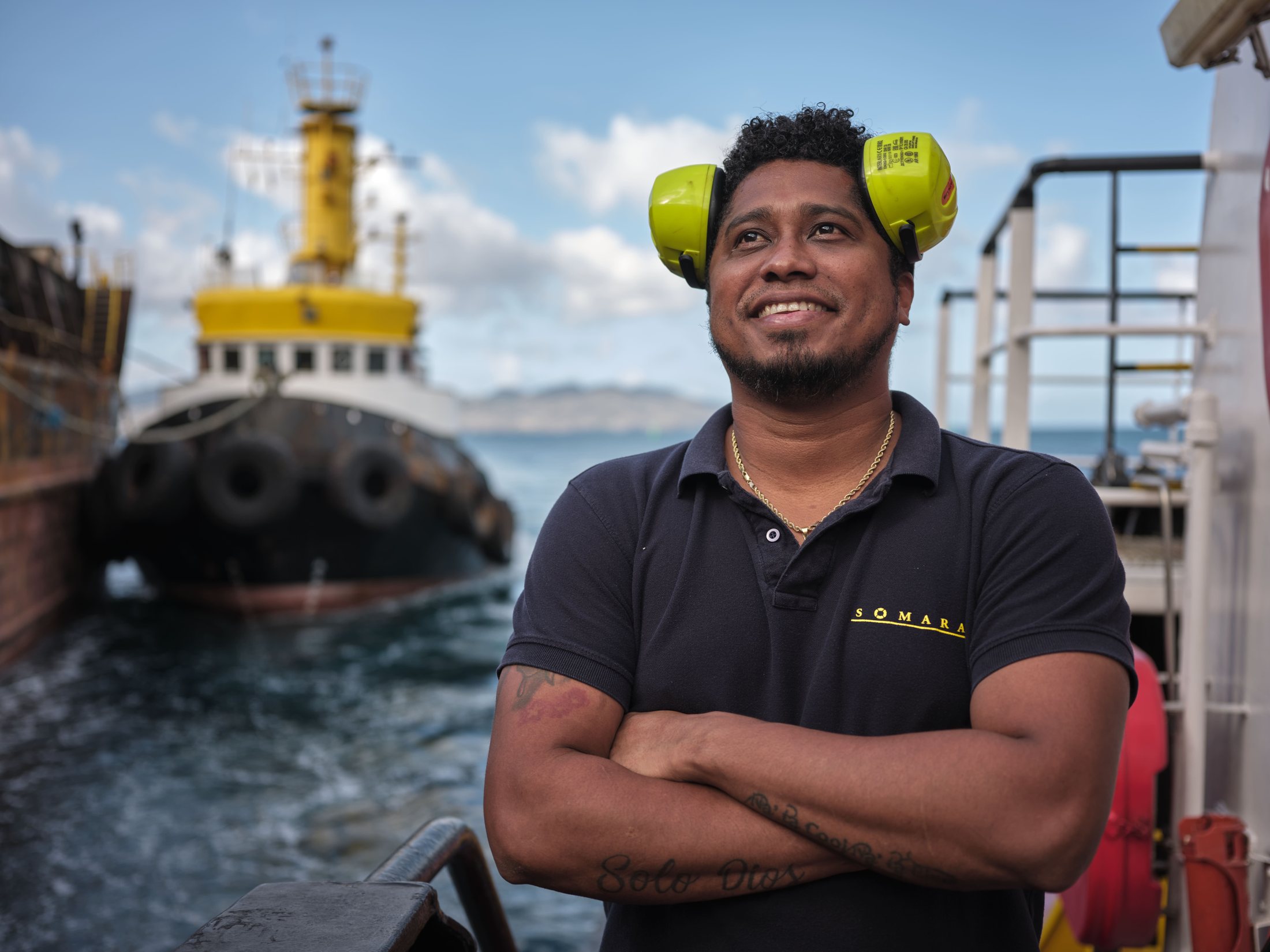Marin de la SOMARA, casque antibruit relevé, un tug en arrière-plan — photographie Romain Cruse
