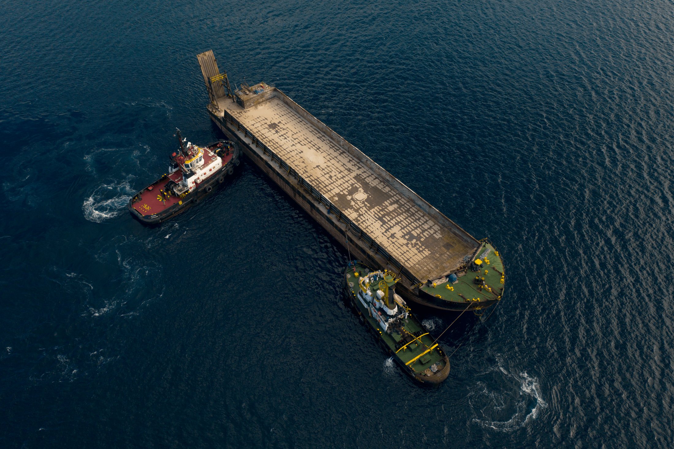 Barge manœuvrée par deux remorqueurs, vue aérienne — photographie Romain Cruse